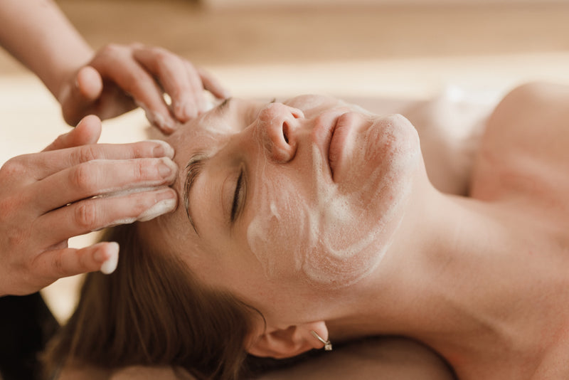 A woman laying down with her eyes closed receiving a facial for healthier skin