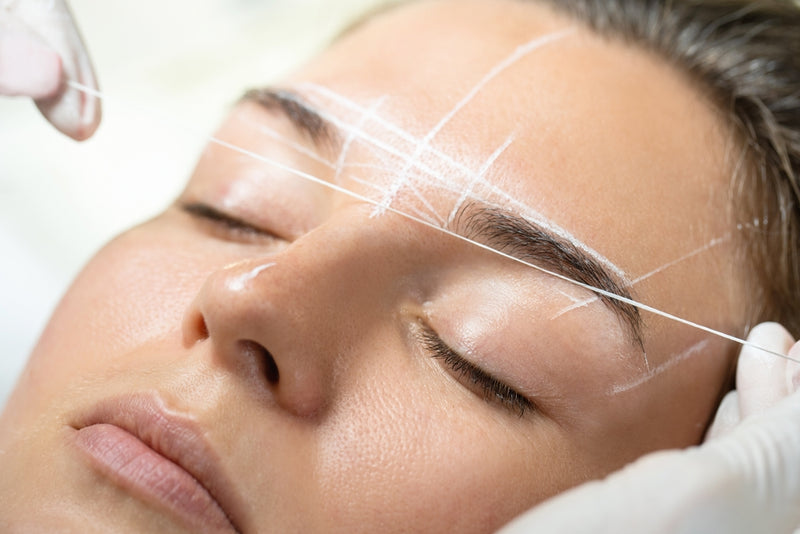 Young woman during professional eyebrow mapping procedure. Brow mapping is done by measuring specific distances and using a thread coated in powder to lay lines on the brows.
